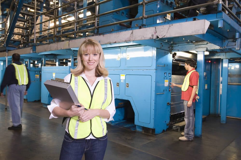 US Manufacturing data woman holding clipboard with operators in background at the factory US Manufacturing data woman holding clipboard with operators in background at the factory