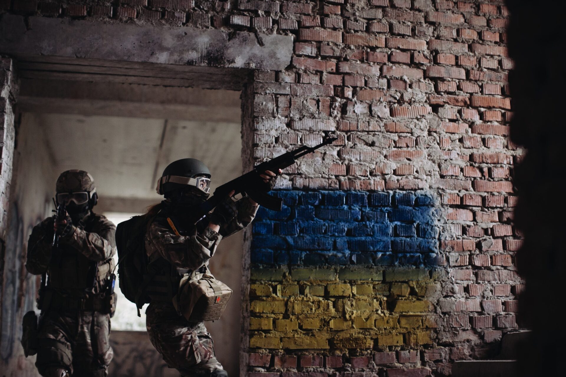 Ukrainian Soldiers military in the war with a weapon in his hands. The flag of Ukraine is painted on a brick wall. Relations between Ukraine and Russia Ukrainian Soldiers military in the war with a weapon in his hands. The flag of Ukraine is painted on a brick wall. Relations between Ukraine and Russia